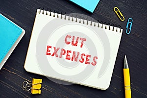 Business concept about CUT EXPENSES with sign on the piece of paper. Cost cuttingÂ refers to measures implemented by a company to